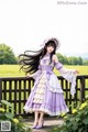 A woman in a purple and white dress standing on a wooden bridge.