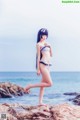 A woman in a bikini standing on a rock by the ocean.