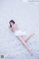 A woman in a white dress laying on the beach.