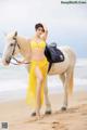 A woman in a yellow bikini standing next to a white horse.