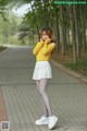 A woman in a yellow sweater and white skirt posing for a picture.