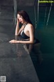 A woman in a black bikini sitting in a pool.