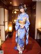 A woman in a blue kimono standing in a hallway.