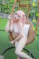 A woman with pink hair sitting in a wicker chair.