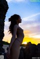 A nude woman standing in front of a sunset.