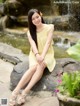 A woman in a yellow dress sitting on a rock by a waterfall.