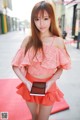 A woman in a pink top and orange skirt holding a tablet.