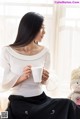 A woman sitting on a window sill holding a cup of coffee.