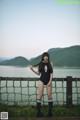 A woman in a black bathing suit standing by a fence.