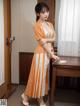 A woman in an orange and white dress standing next to a desk.