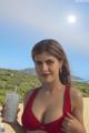 A woman in a red bikini holding a drink on the beach.